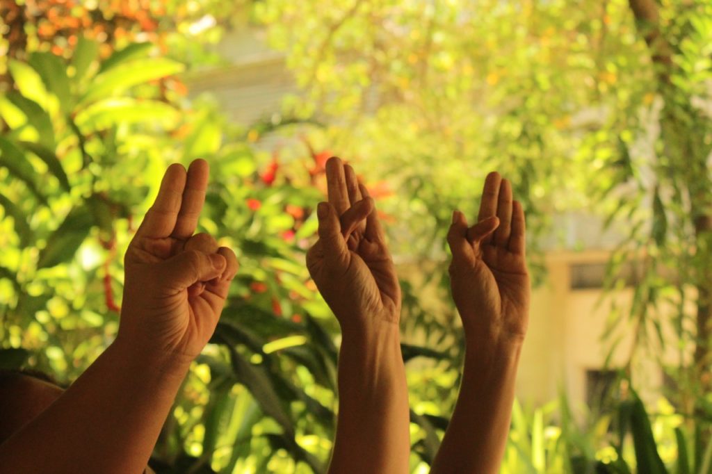 Esta imagem contém três mãos soletrando "U-F-F" em Libras, que é a sigla da Universidade Federal Fluminense.